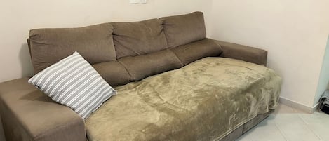 A brown sofa with a striped pillow, a blanket, and a wall outlet.