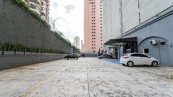 A parking area with two cars, a building with a blue door, and a tall pink building in the background.