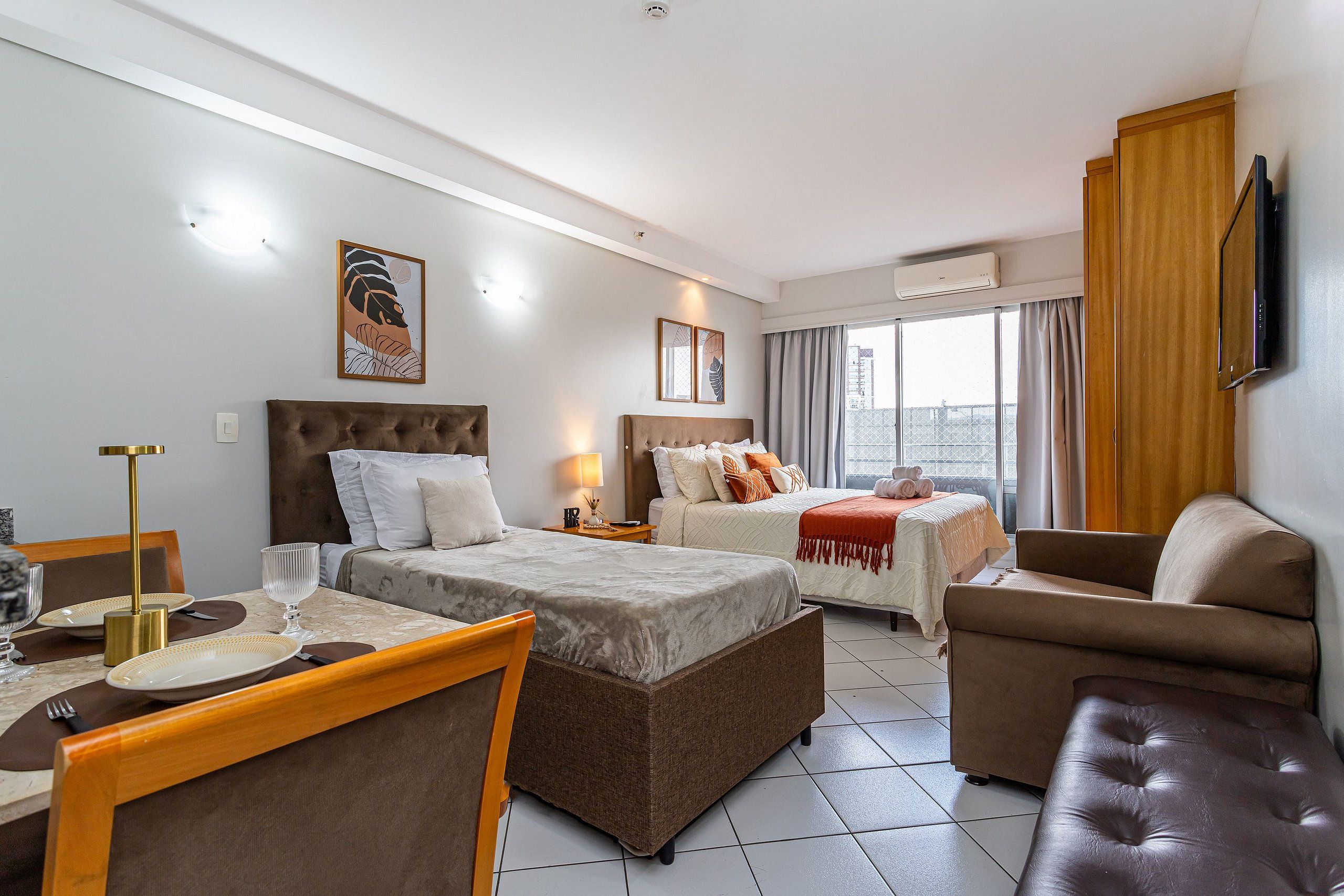 A hotel room with two beds, a sofa, a dining table with chairs, and a TV.