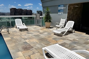 A rooftop lounge area with lounge chairs, a potted plant, and a poolside view of a cityscape. - Perdizes Residence Flat Condomínio  (São Paulo)