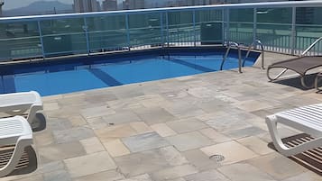 A rooftop pool with clear blue water, surrounded by stone tiles and white lounge chairs.