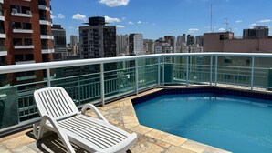 A rooftop pool with a clear view of the city skyline, a white lounge chair, and a glass railing. - Perdizes Residence Flat Condomínio  (São Paulo)