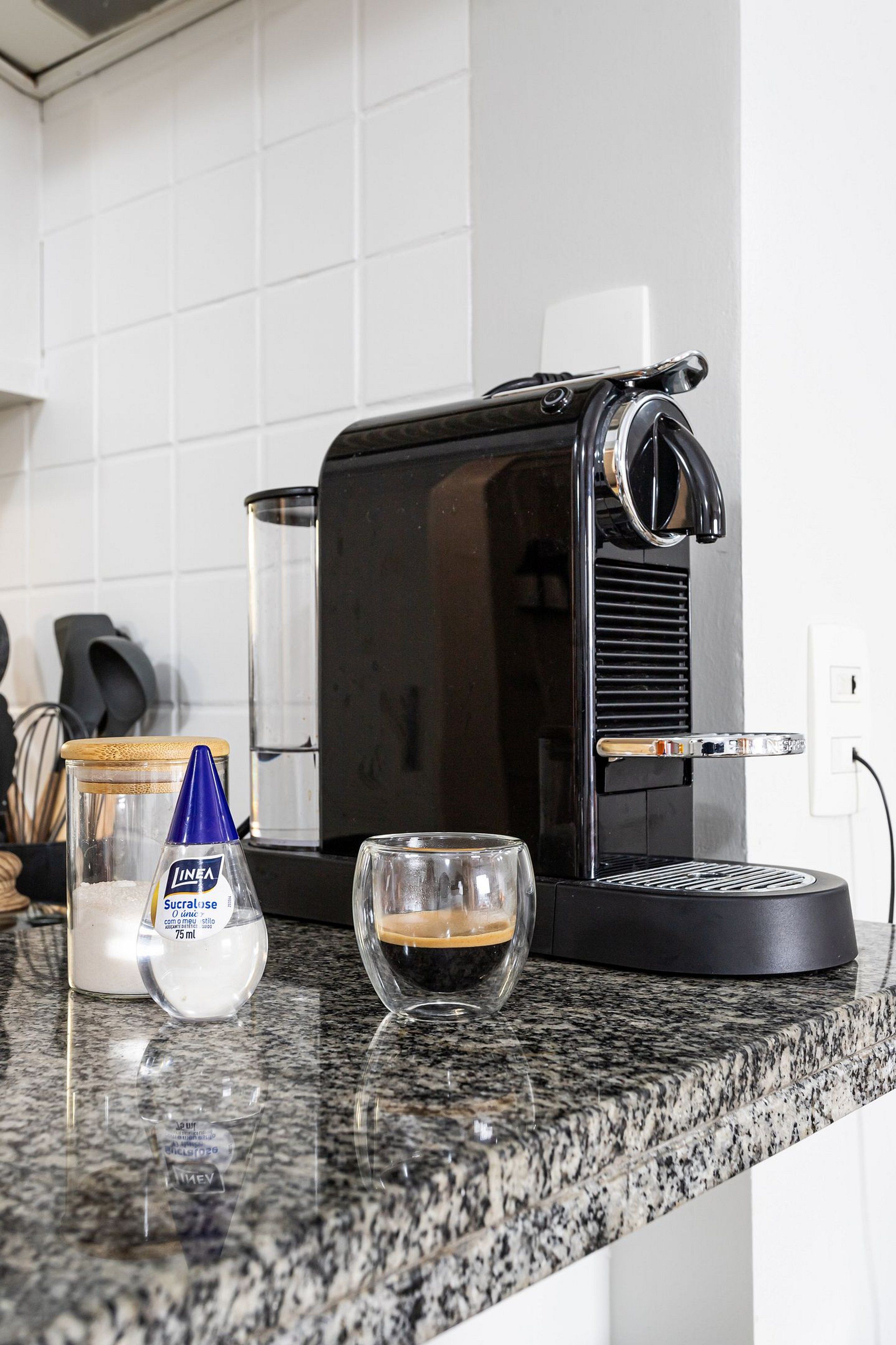 Een keuken met een koffiezetapparaat, een glazen pot en een glazen beker op een granieten aanrecht.