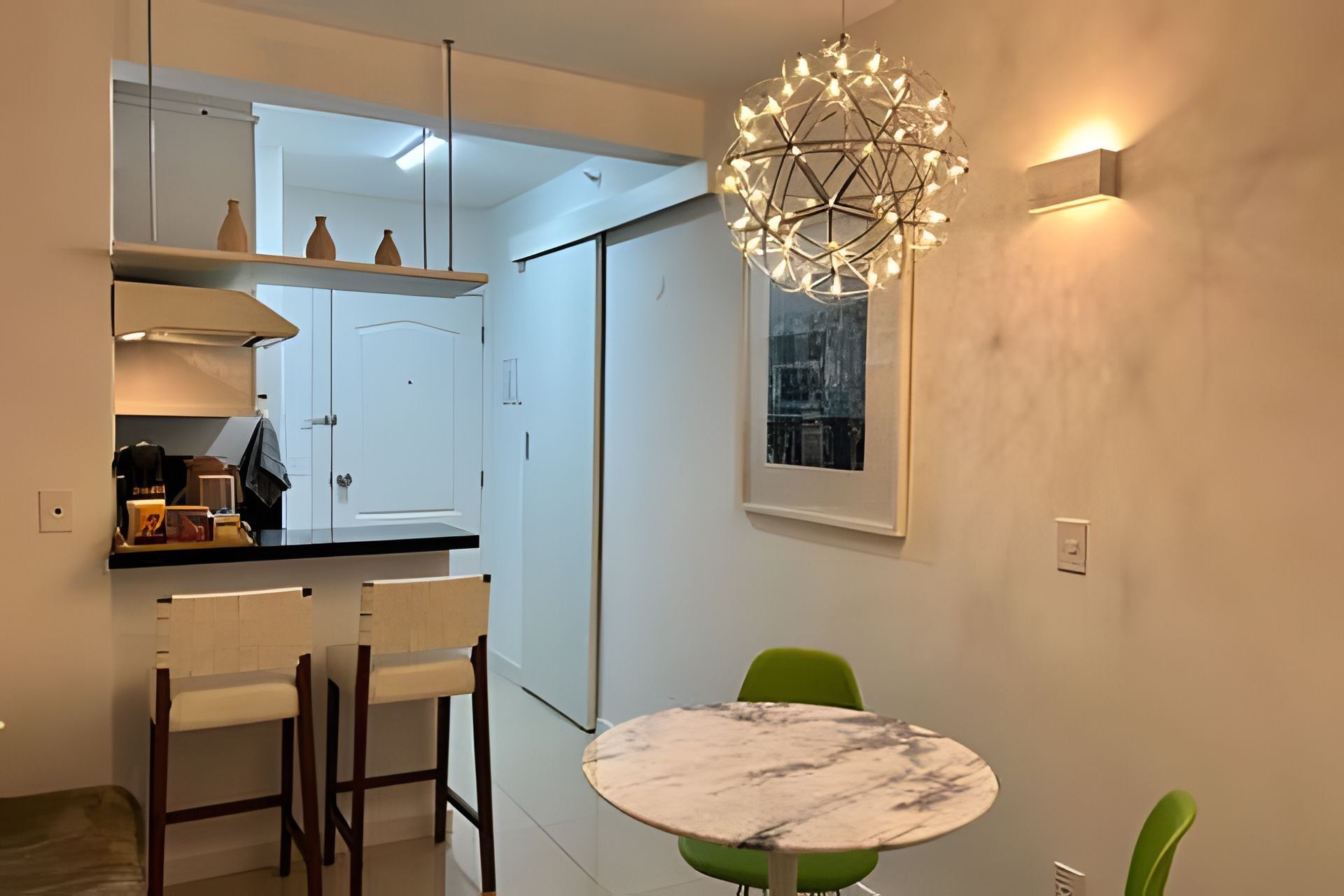 A modern kitchen with white cabinets, a marble countertop, and a unique spherical light fixture.