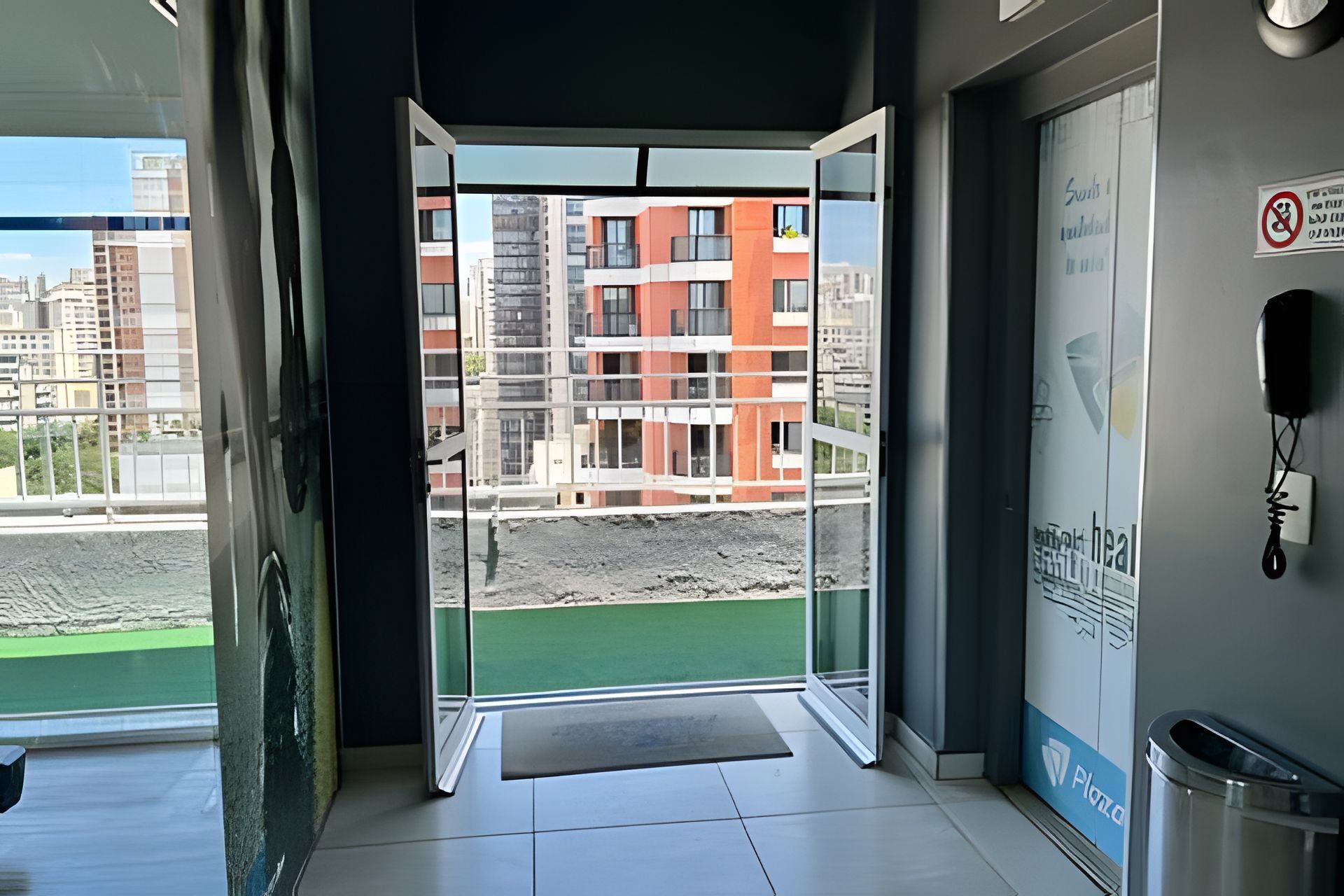 A hotel entrance with a glass door leading to a balcony with a view of a building under construction.