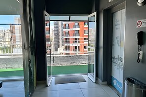 Entrada de hotel con puerta de cristal que da a un balcón con vistas a un edificio en construcción.