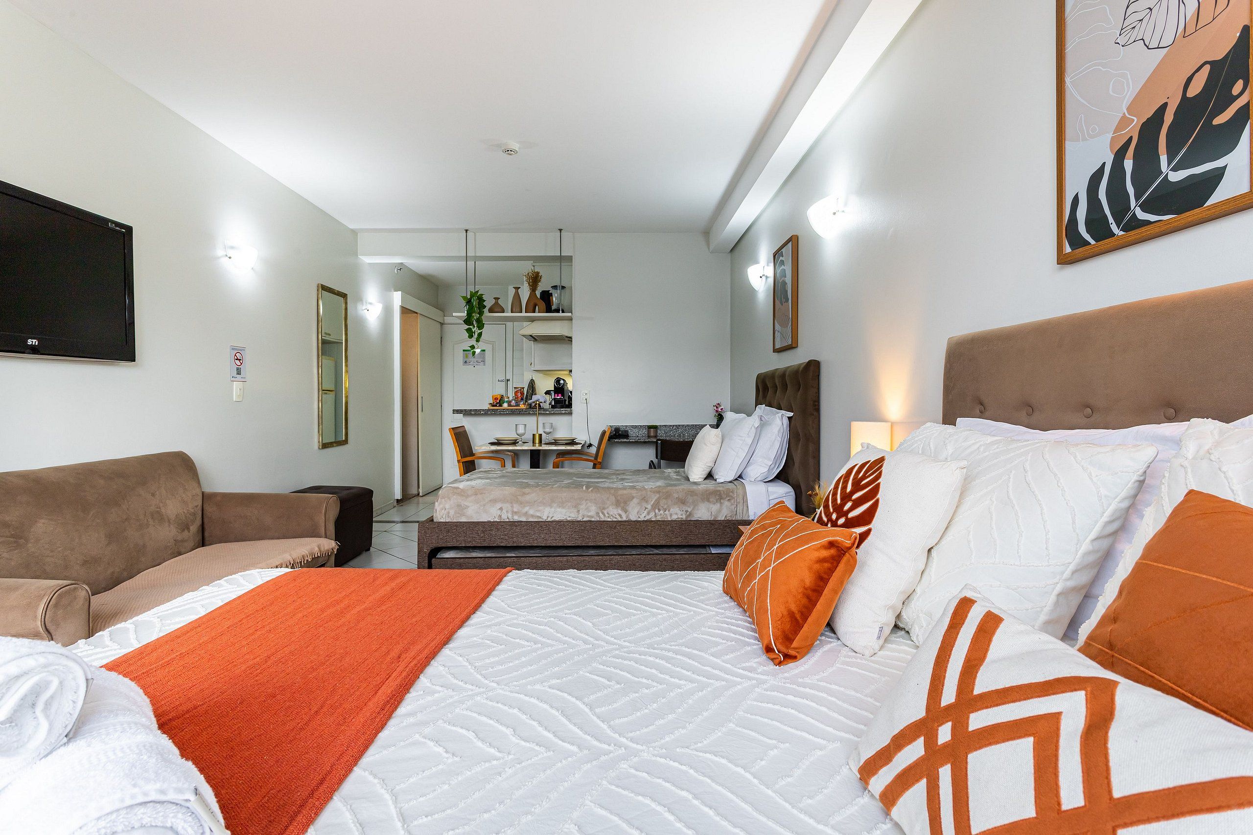 Quarto de hotel com cama, sofá, escrivaninha e cozinha compacta.