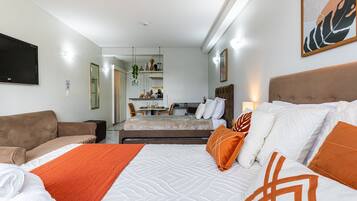Quarto de hotel com cama, sofá, escrivaninha e cozinha compacta.
