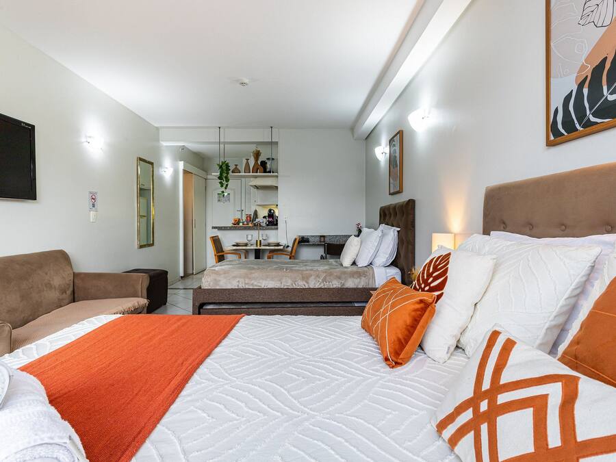 Ett hotellrum med en säng, en soffa, ett skrivbord och ett litet kök.