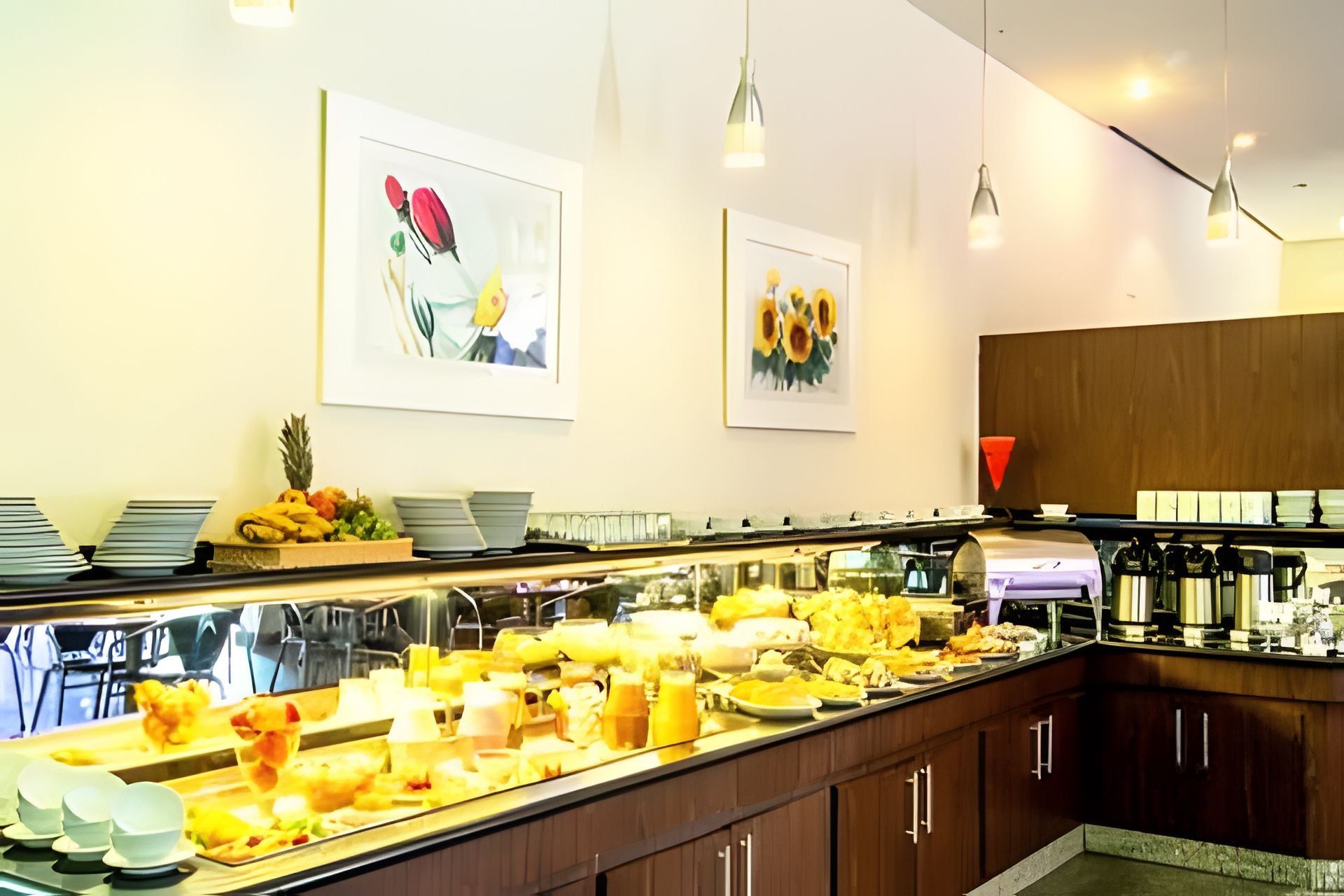 Ein Buffet mit verschiedenen Speisen, eine Kaffeestation und zwei gerahmte Blumenbilder an der Wand.