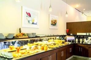 A buffet with various food items, a coffee station, and two framed floral paintings on the wall. - Perdizes Residence Flat Condomínio  (São Paulo)