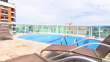 A rooftop pool with clear blue water, a glass balustrade, and two lounge chairs.