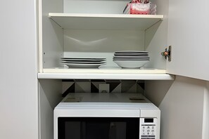 Una cocina con microondas, una estantería con platos apilados y un armario con pomo.
