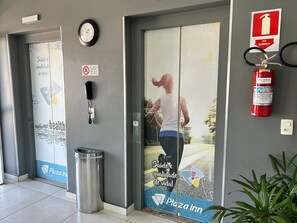 A hotel entrance with a sign for Plaza Inn, a fire extinguisher, a phone, and a trash bin. - Perdizes Residence Flat Condomínio (São Paulo)