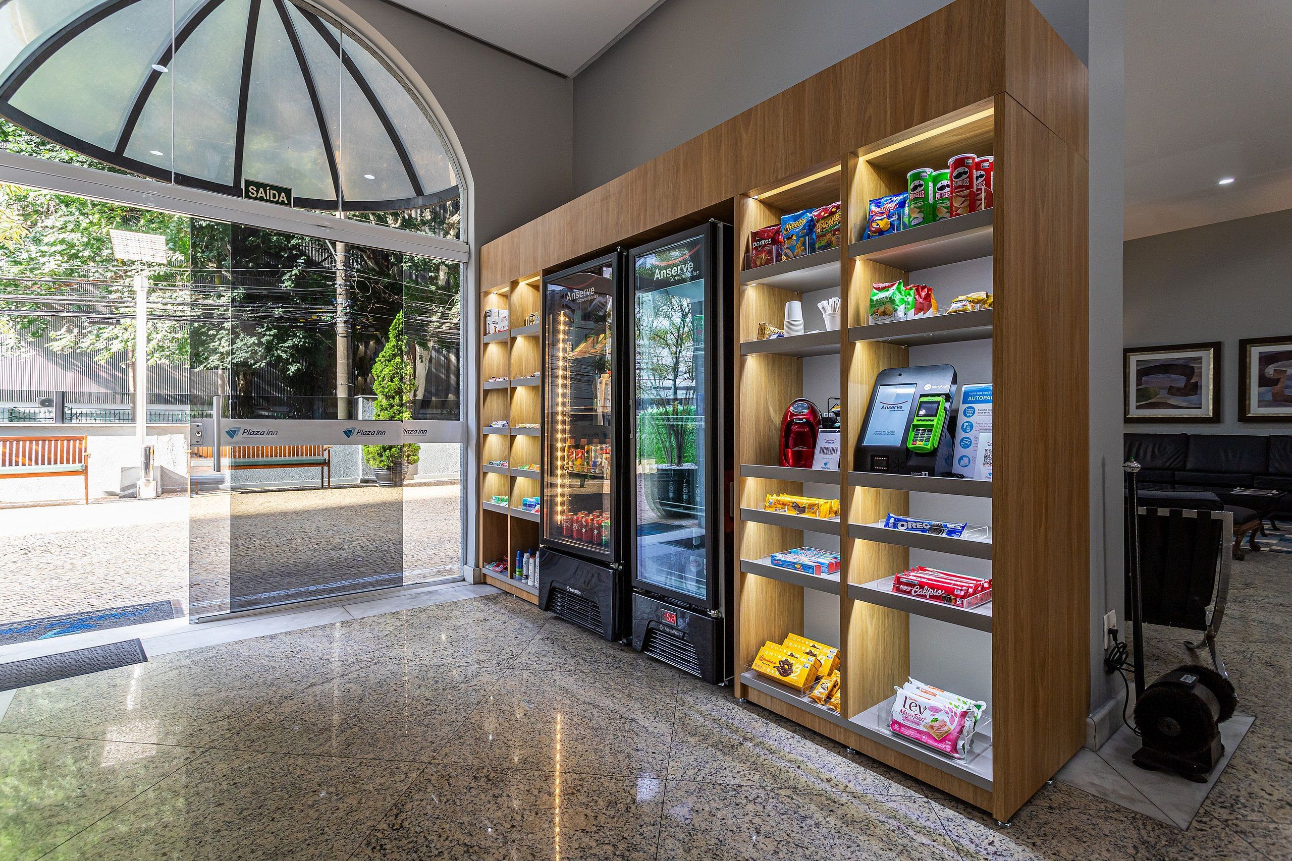 Interior moderno com entrada de vidro, balcões refrigerados e prateleiras repletas de lanches e bebidas.