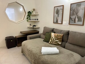 A living room with a sofa, a coffee table, a side table, a potted plant, and a wall-mounted shelf with decorative items. - Perdizes Residence Flat CondomĂnio (SĂŁo Paulo)