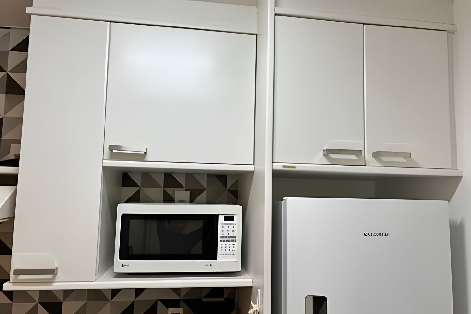 A kitchen with white cabinets, a microwave, and a refrigerator.