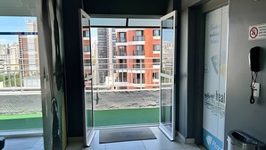 A hotel entrance with a glass door leading to a balcony with a view of a building under construction. - Perdizes Residence Flat Condomínio  (São Paulo)
