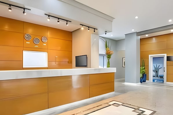 A reception desk with a flat-screen TV, a whiteboard, and a vase with flowers.