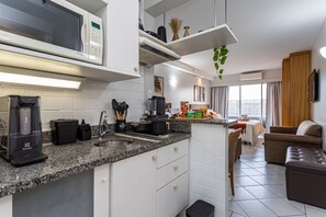 A modern kitchen with a microwave, coffee maker, and a sink. There is a dining area with a sofa and a TV. - Perdizes Residence Flat CondomÃnio (São Paulo)