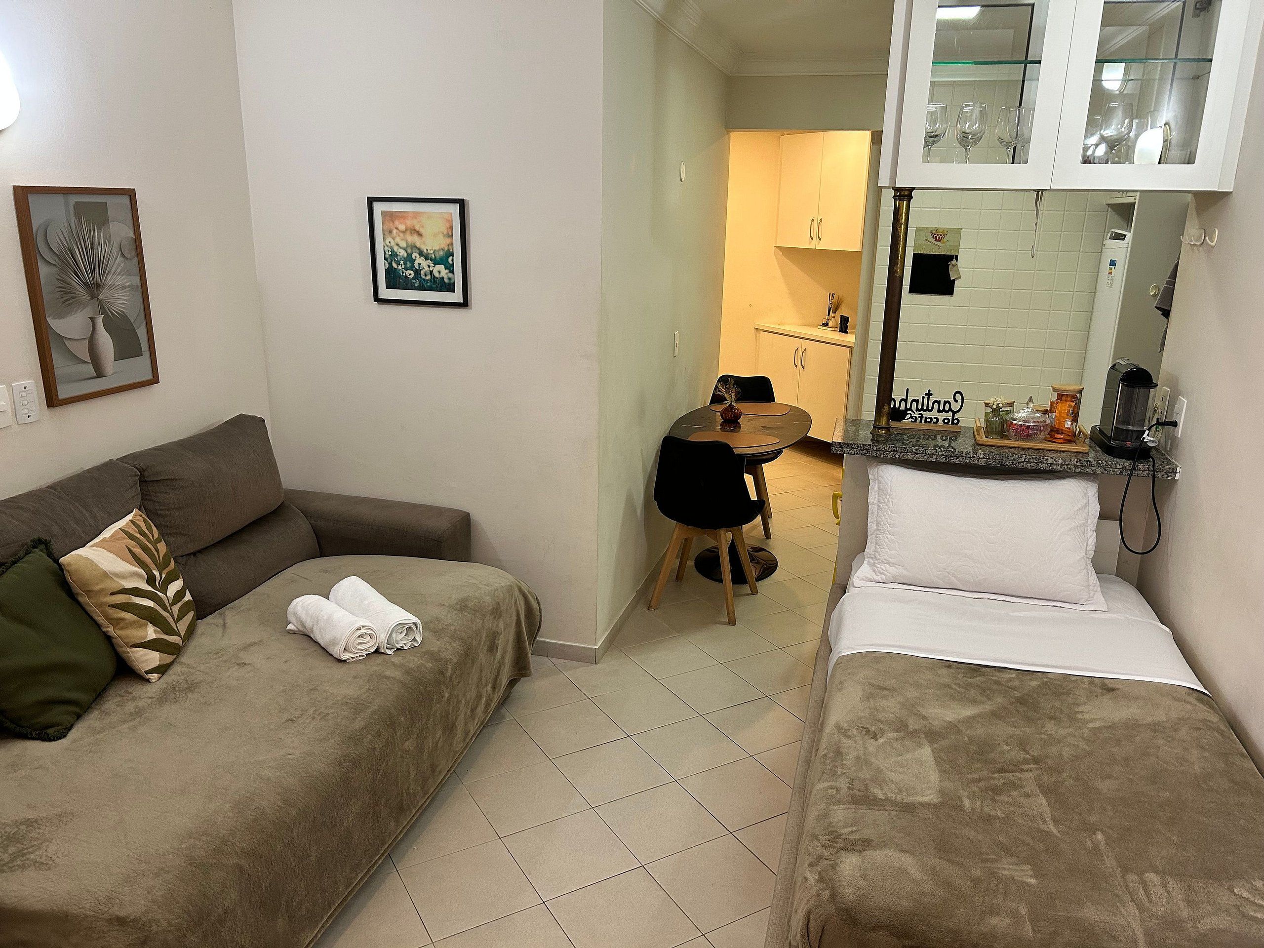 A room with a sofa, a bed, a dining table, and a kitchen area.