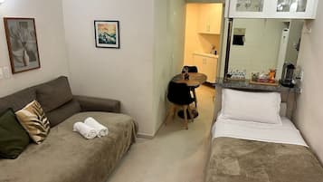 A room with a sofa, a bed, a dining table, and a kitchen area.