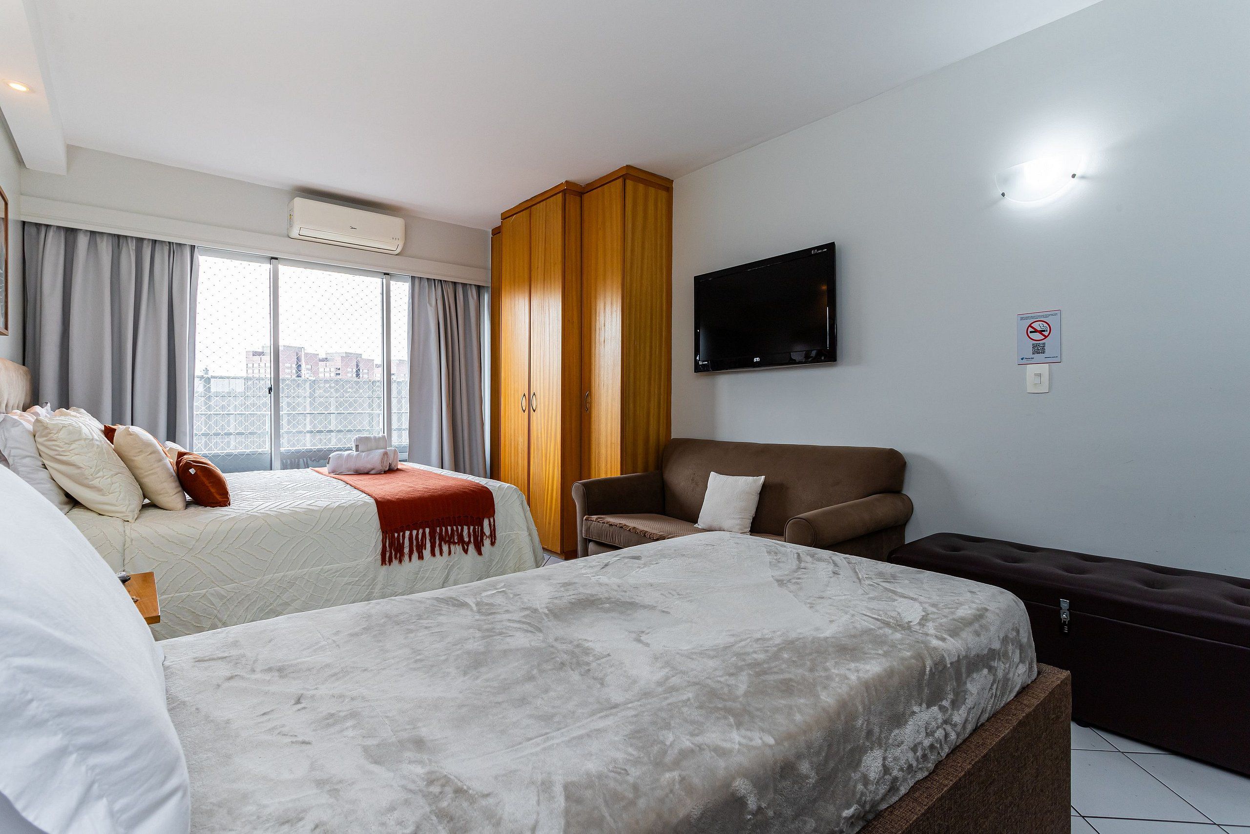 A hotel room with two beds, a TV, and a view of the city.