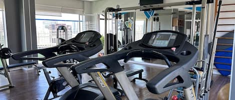 Un gimnasio con cintas de correr, máquinas de pesas y un ventanal grande.