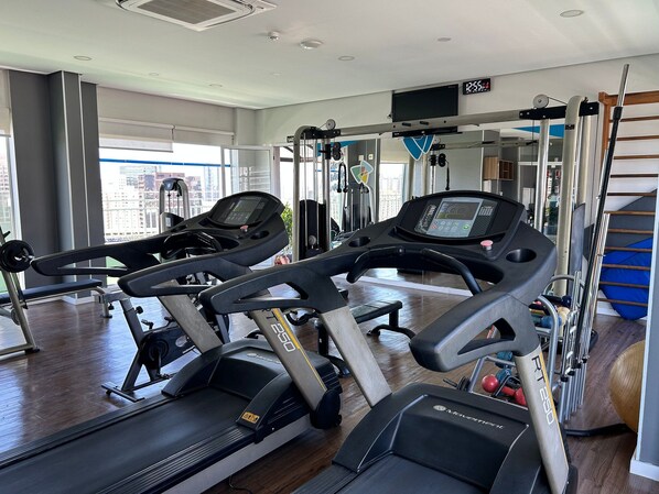 Un gimnasio con cintas de correr, máquinas de pesas y un ventanal grande.