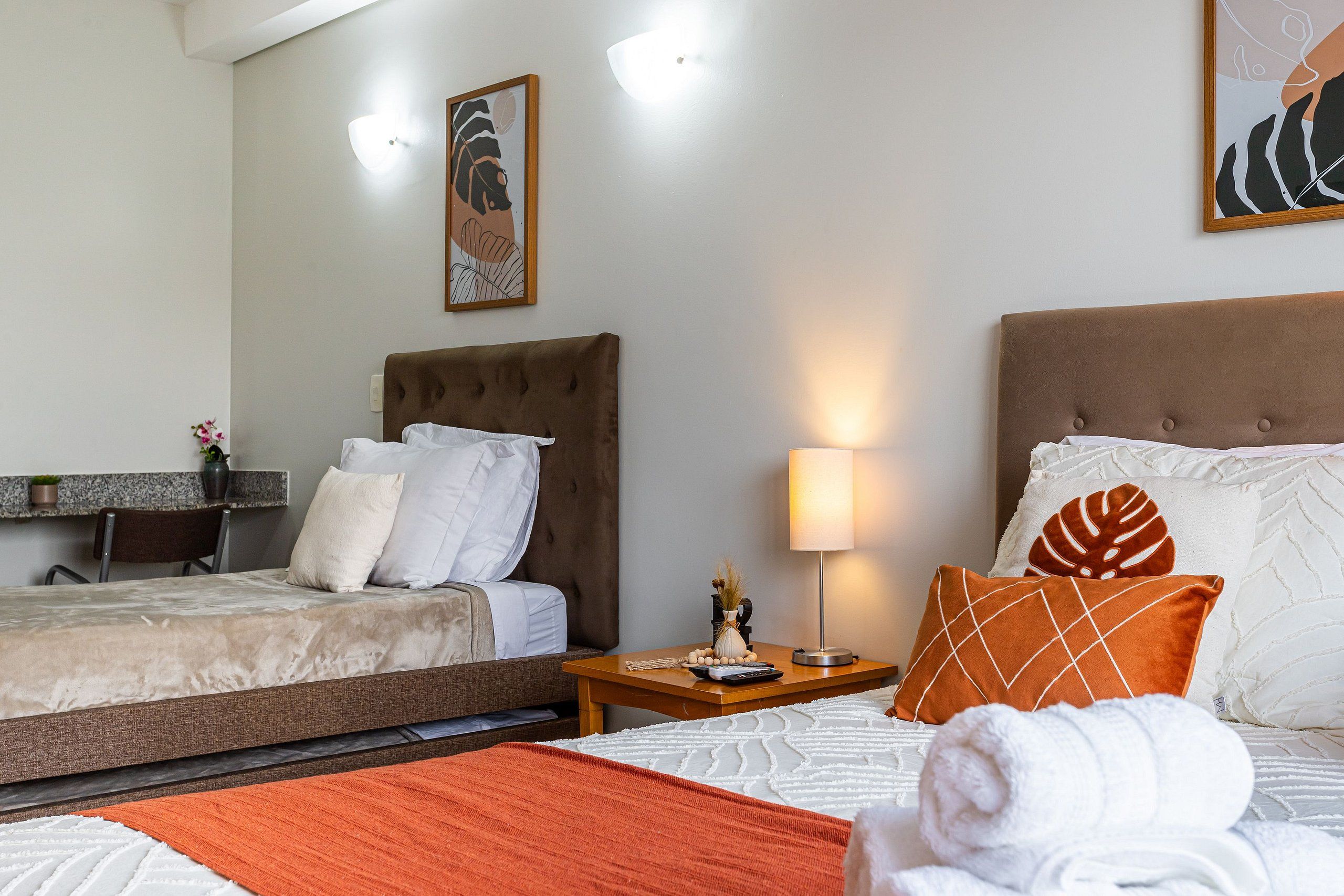 A hotel room with two beds, a desk, a lamp, and artwork on the walls.