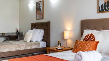 A hotel room with two beds, a desk, a lamp, and artwork on the walls.