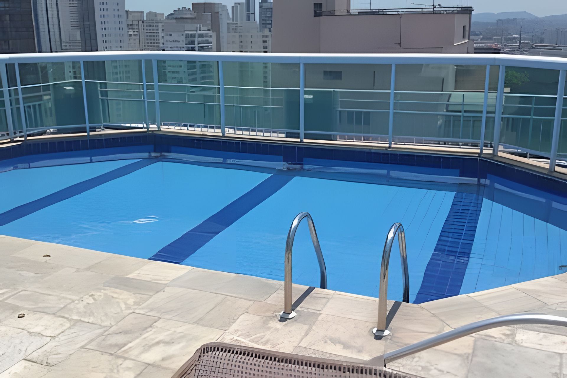 A rooftop swimming pool with clear blue water, metal pool ladders, and a glass railing.