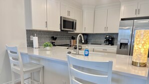 Cocina moderna con armarios blancos, refrigerador de acero inoxidable, microondas y una isla integrada con taburetes de bar.