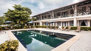 A pool area with lounge chairs and umbrellas, a building with balconies, and a clear sky.