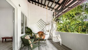 A balcony with a wooden floor, a green chair, a small table, and a hanging hammock.