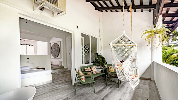 A modern interior with a wooden floor, green chairs, a hanging chair, and a white bathtub.