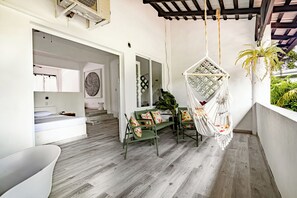 Un interior moderno con piso de madera, sillas verdes, una silla colgante y una bañera blanca.