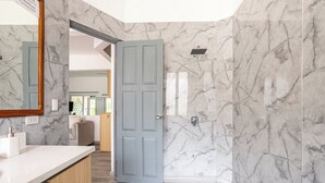 A bathroom with marble walls, a wooden vanity, and a door leading to another room.