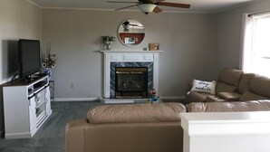 Un salon avec une cheminée, un téléviseur, un canapé et un ventilateur de plafond.