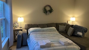 Une chambre à coucher comprenant un lit, un canapé, deux lampes de chevet, une fenêtre et un élément décoratif mural.