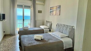 Una camera d'albergo con due letti, una televisione, vista mare e un quadro appeso al muro.