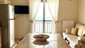Un'area pranzo con tavolo, sedie, una ciotola di frutta, televisore e divano.