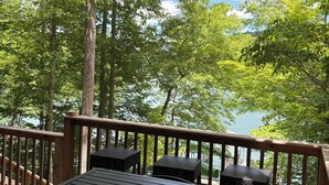 Een houten terras met een tafel en stoelen, uitkijkend op een meer met bomen.