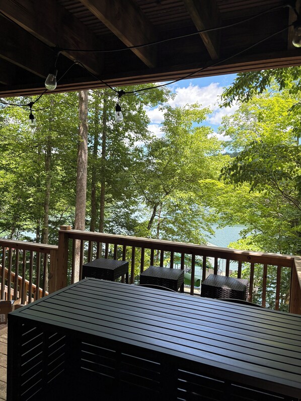 A wooden deck with a table and chairs, overlooking a lake with trees.