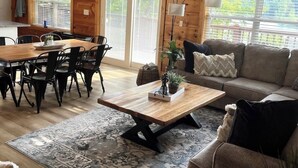 Een gezellig interieur van een chalet met een eethoek, een bank en een grote houten klok aan de muur.
