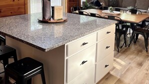 Een keuken met granieten aanrechtbladen, witte kastjes en een klok aan de muur.
