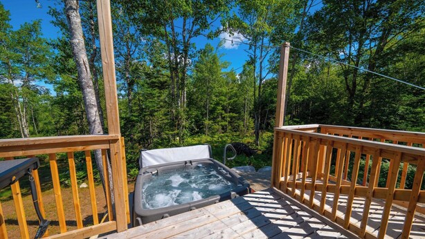Une terrasse en bois avec un jacuzzi, le tout entouré d’arbres.