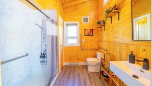 Une salle de bain moderne et compacte, dotée d’une douche, de toilettes et d’un lavabo, avec des murs en bois et une zone de douche carrelée en marbre.