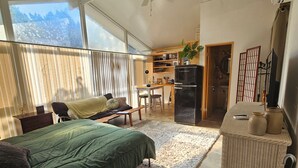 Une pièce spacieuse comprenant un lit, un petit coin salon, une kitchenette et une grande fenêtre.