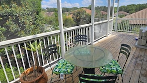 Une terrasse extérieure couverte, dotée d’une table et de chaises en verre, et entourée d’une balustrade blanche.